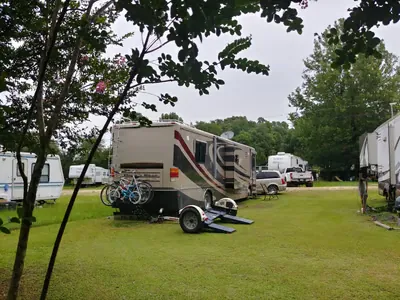 A motorhome with bikes on the back parked on a shady site